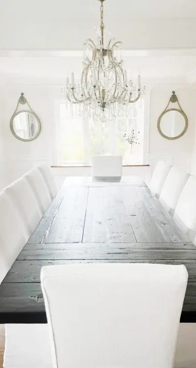 Wood dining table with 10 white chairs and a chandelier above